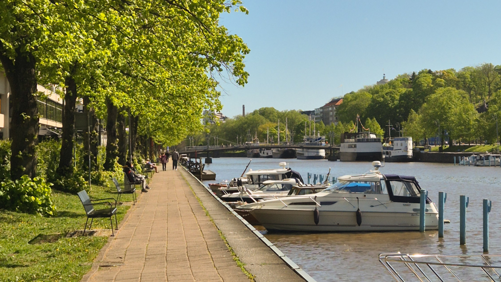 Summer day view of Aura River in Turku, Finland with boats and green trees along the shore.