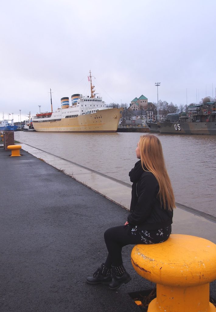 Me sitting by the Aura River in Turku, Finland with Hostel s/s Bore visible in the background.