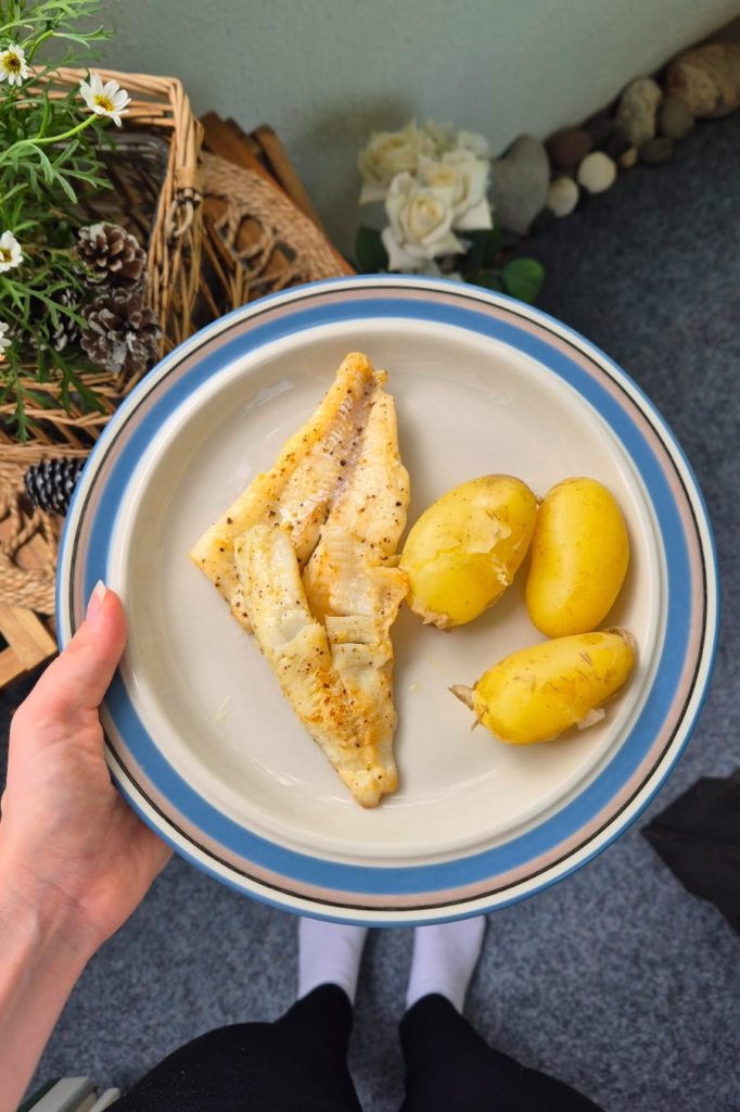 Sofia holding a plate with freshly boiled new potatoes and fish caught from the sea, enjoying a Finnish summer meal.