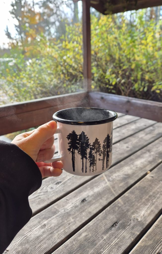 Person holding a cup of coffee while enjoying a peaceful view of a Finnish national park.