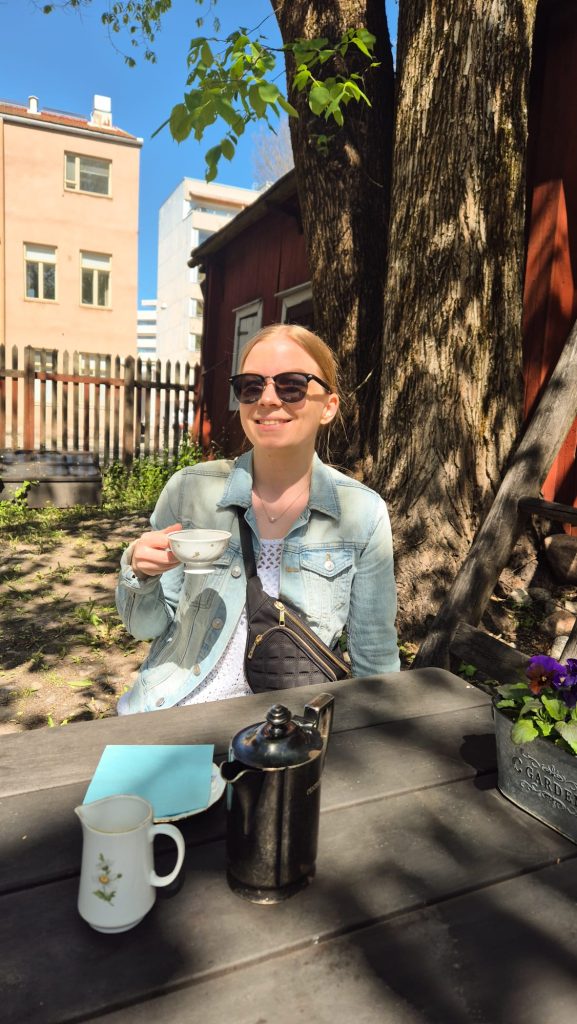 Me smiling and drinking coffee at Café Qwensel in Turku, Finland on a sunny summer day.