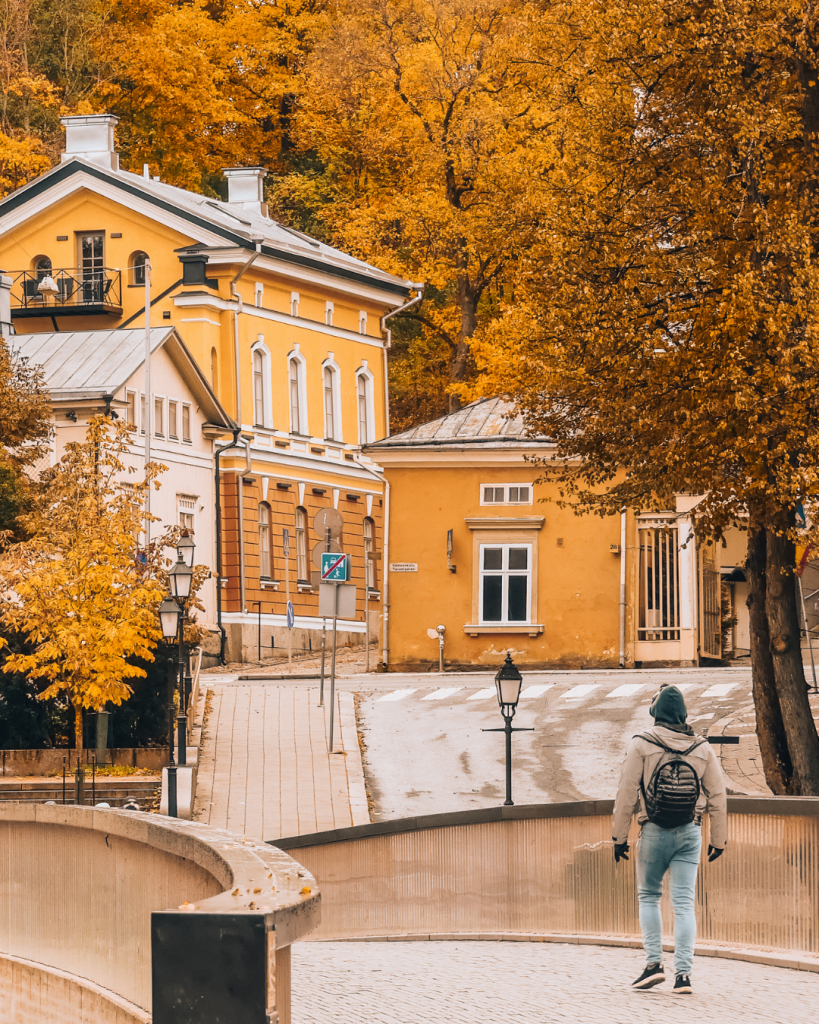 Person walking across a bridge over the Aura River in Turku, with colorful autumn trees and historic buildings in the background.