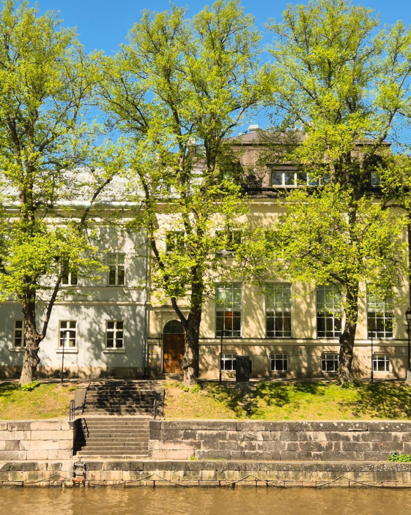 Historic buildings along the Aura River in Turku surrounded by green trees on a sunny summer day.