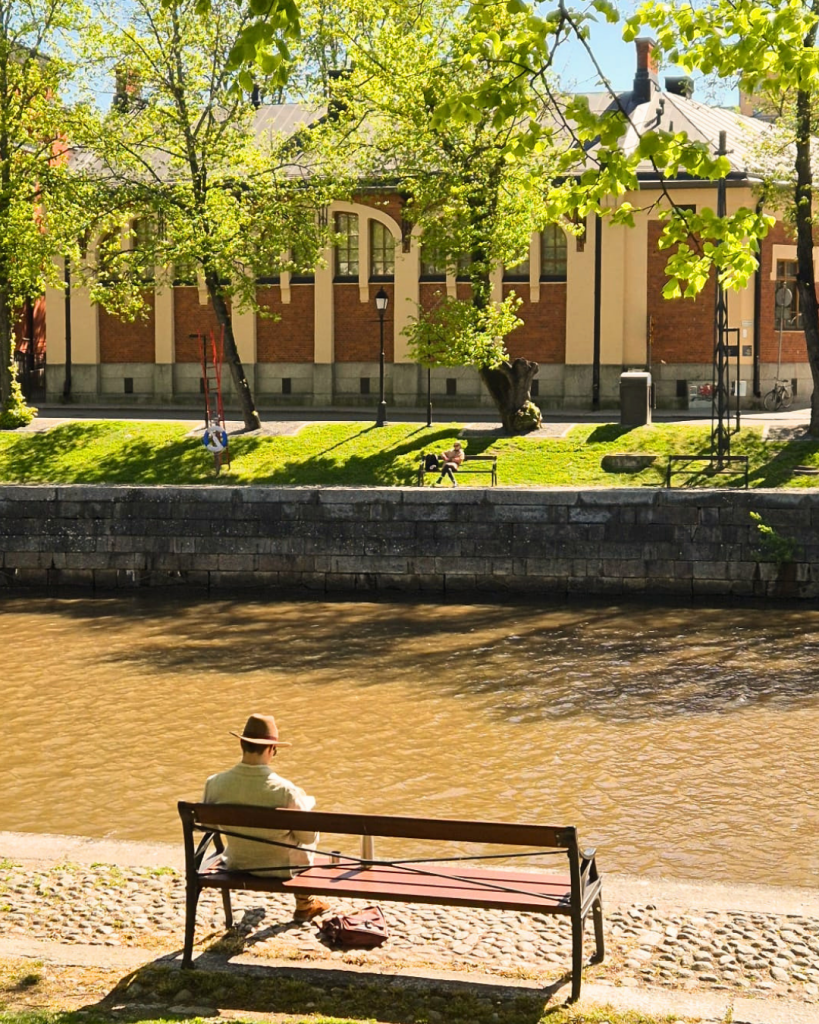 Man sitting on a bench overlooking the Aura River on a peaceful summer day in Turku, Finland.