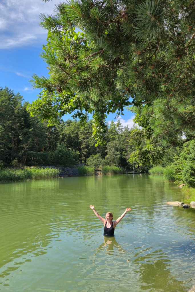 Person swimming at a Finnish summer cottage surrounded by nature on a sunny summer day.