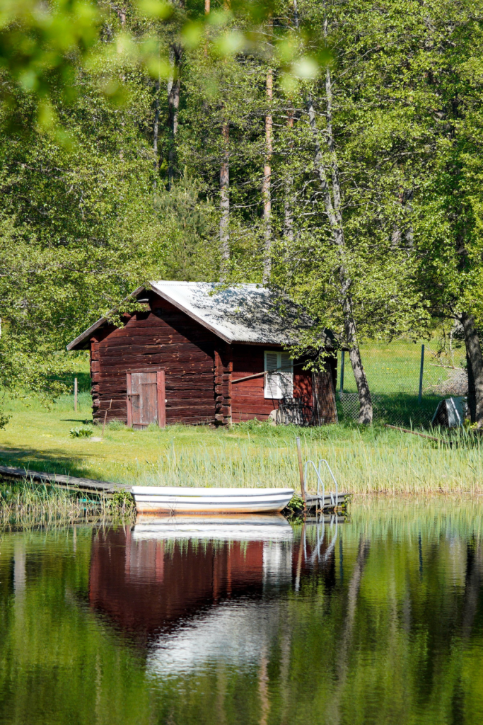 Peaceful coastal scene featuring a red cottage, a boat by the shore, and unspoiled nature.