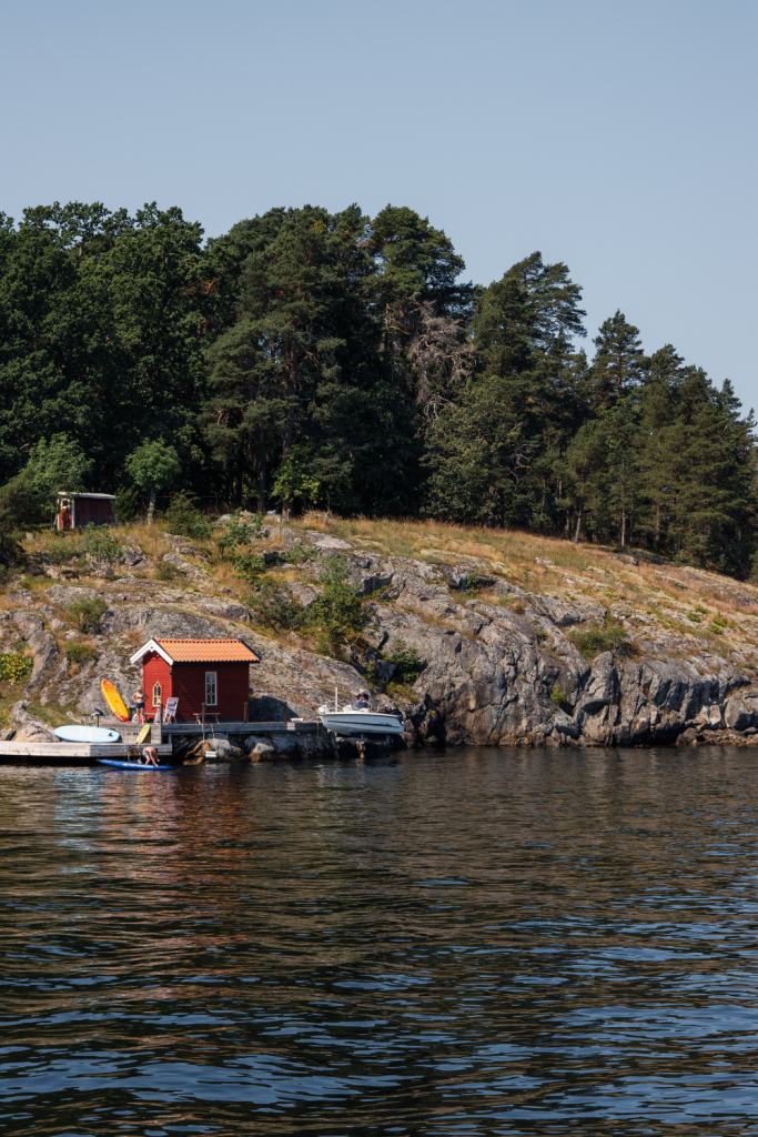 People enjoying a summer day in Finland's archipelago, with rocky shores, the sea, and a small cottage in the background.