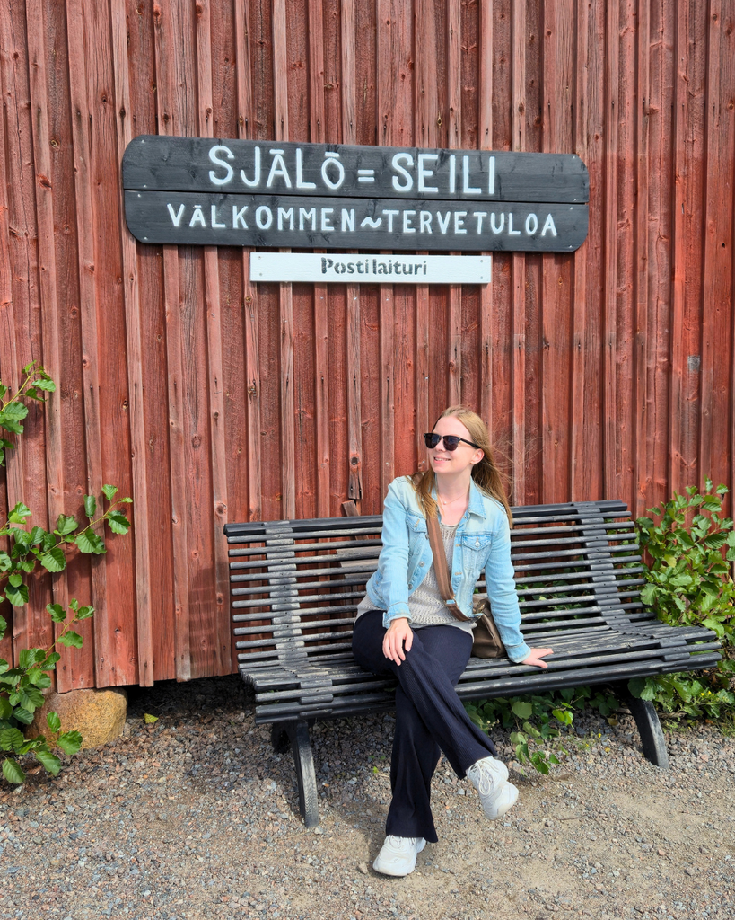 Woman sitting near the Seili Island sign upon arriving on Seili Island in the Finnish Archipelago.