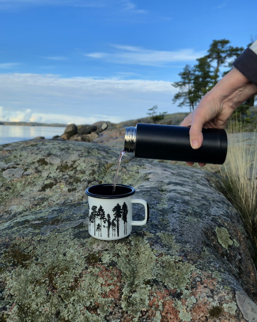 Pouring a drink into a cup on rocks during an autumn hike in the Finnish archipelago, surrounded by Finnish nature and sea views.