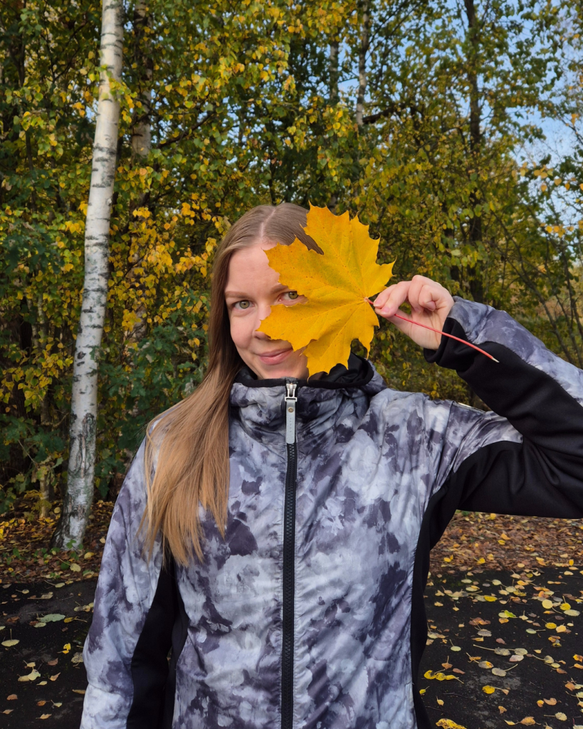Woman holding a colorful autumn leaf in front of her face on an autumn day in Finland.