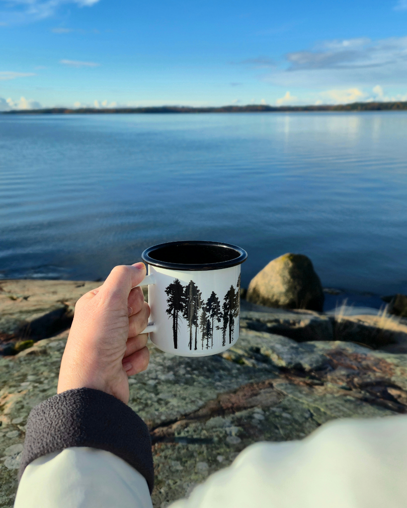 Woman holding a warm cup by the water with a sea view on an autumn day in Finland.