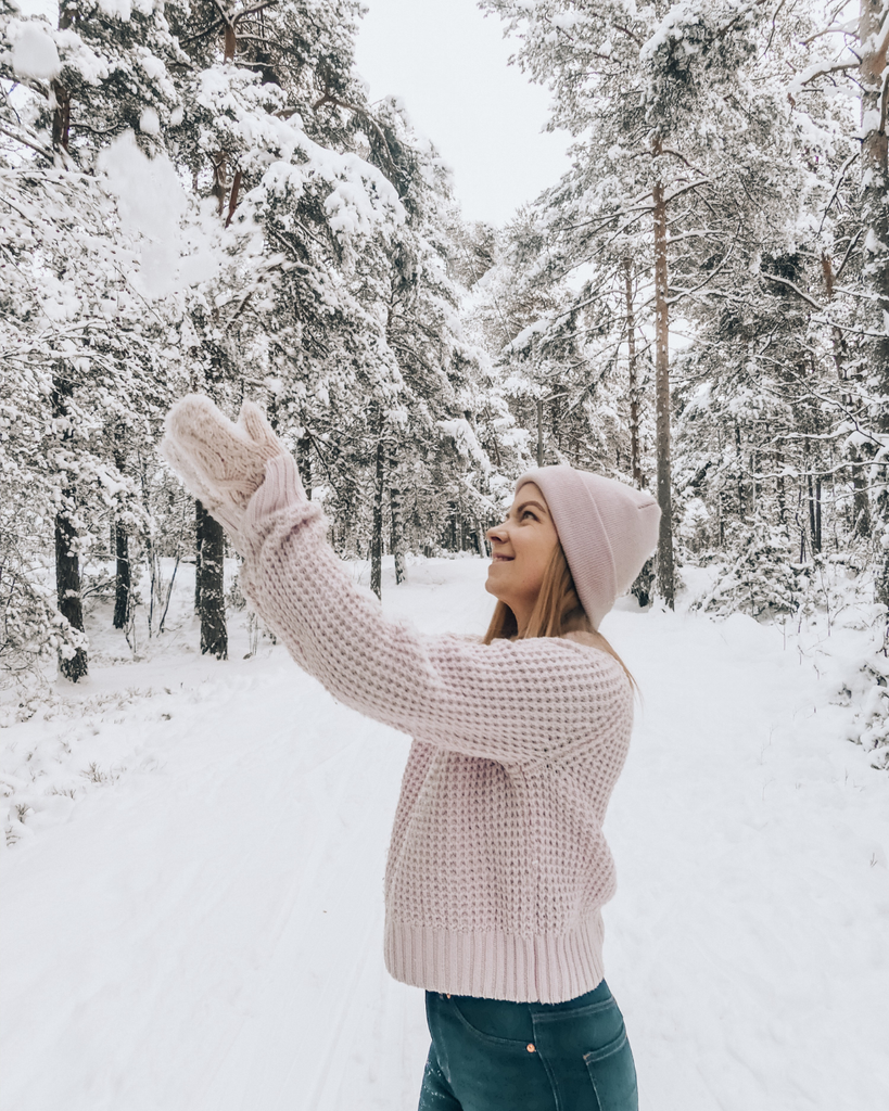 A person throwing snow into the air in front of a snow-covered Finnish forest in winter.