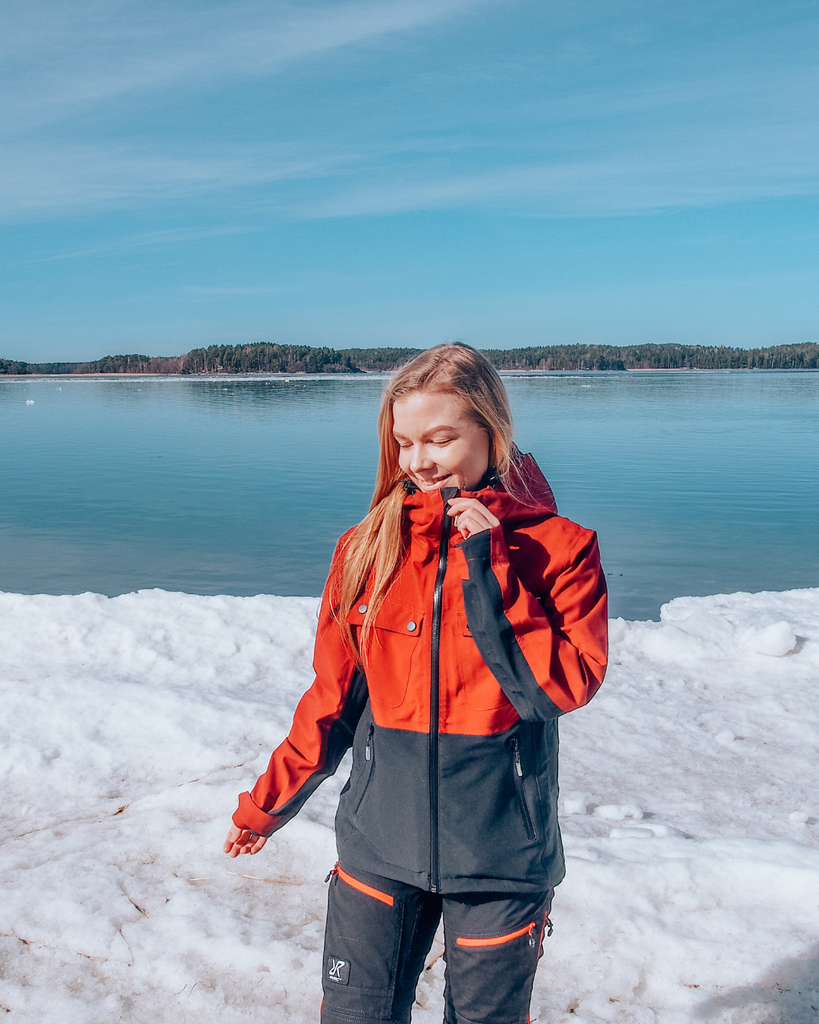 A person wearing a winter jacket standing by the sea on a snow-covered shoreline in Finland.