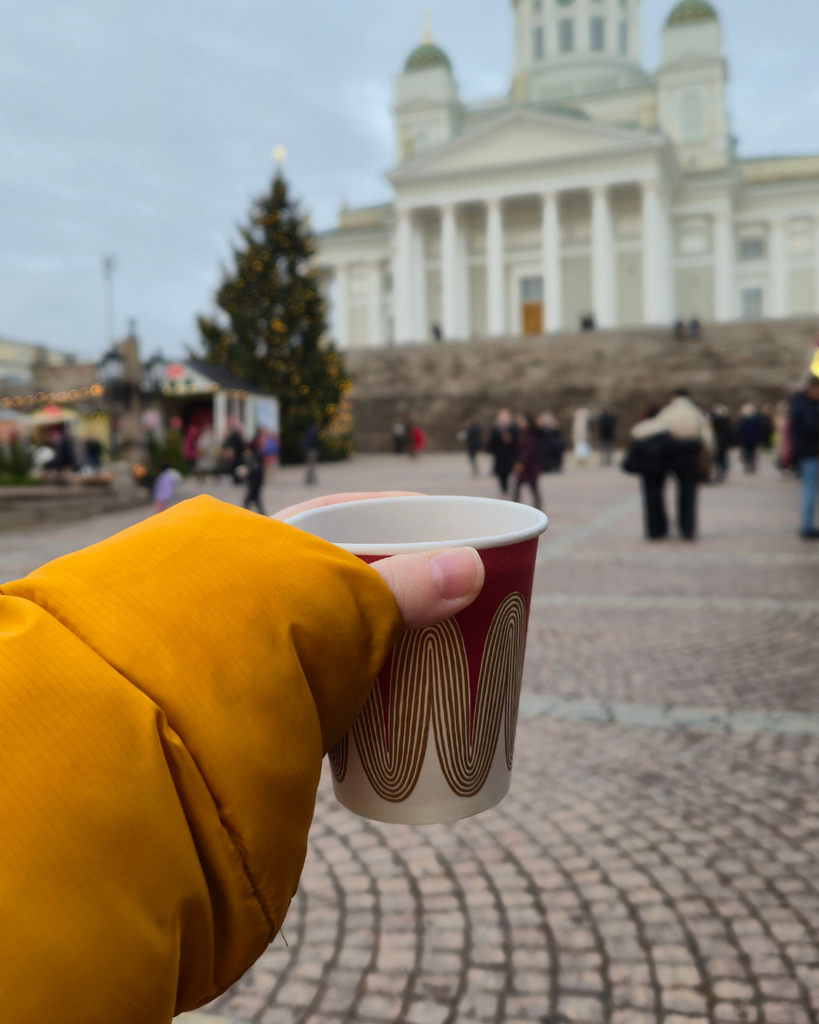 Holding a mug of glögi in front of Helsinki Cathedral during winter.