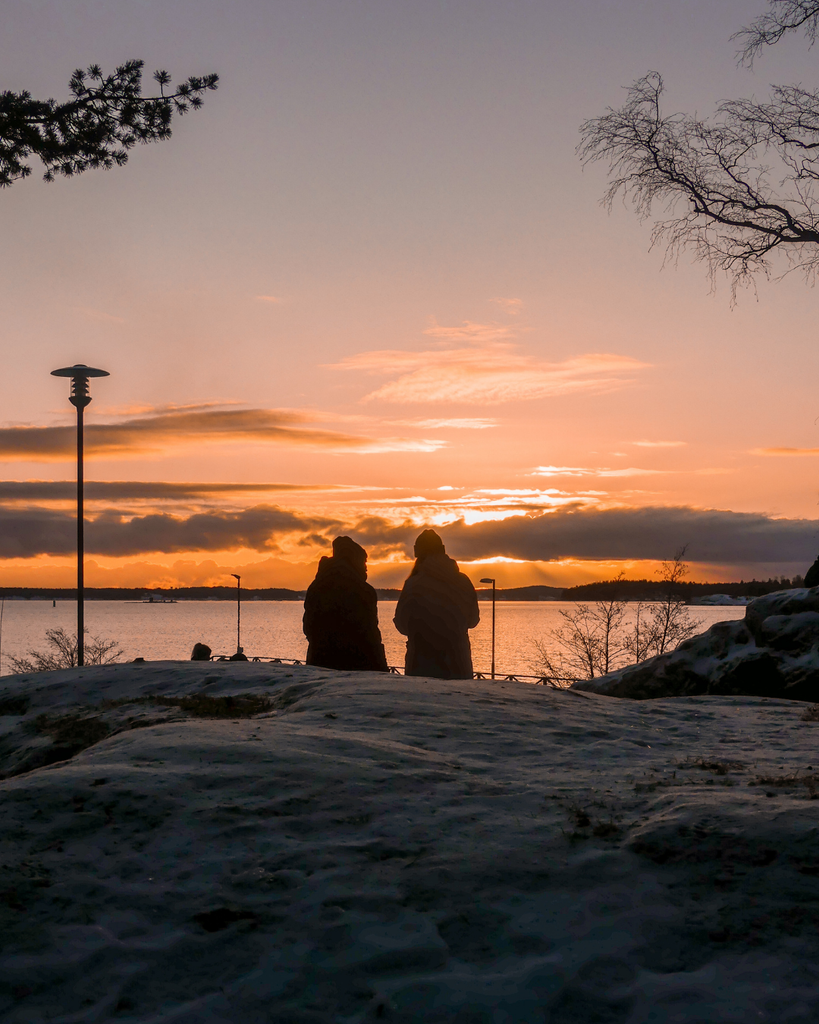 Two people sitting on rocks by the sea, watching the winter sunset in Ruissalo, Turku.