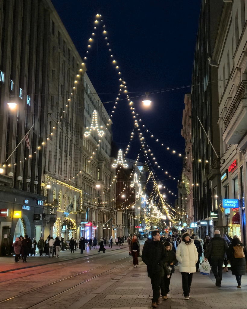 People walking along a Helsinki street in winter, with festive lights illuminating the city in the evening.