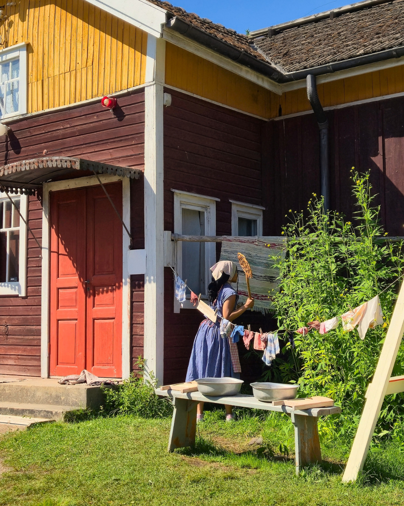 Woman dressed in traditional clothing carrying out everyday tasks at Kuralan Kylämäki open-air museum in Turku, Finland.